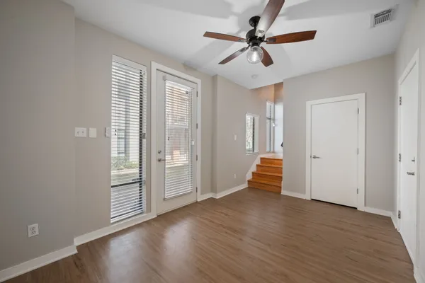an empty room with wooden floor chandelier fan and windows