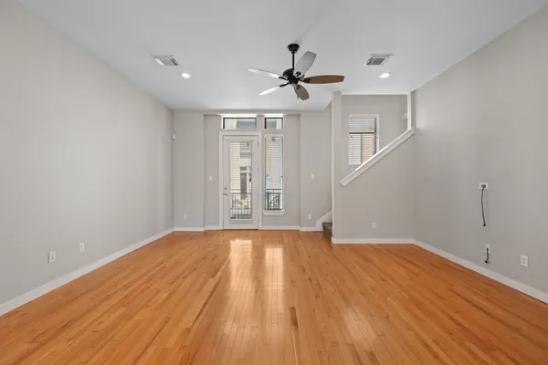 a view of an empty room with wooden floor and a ceiling fan