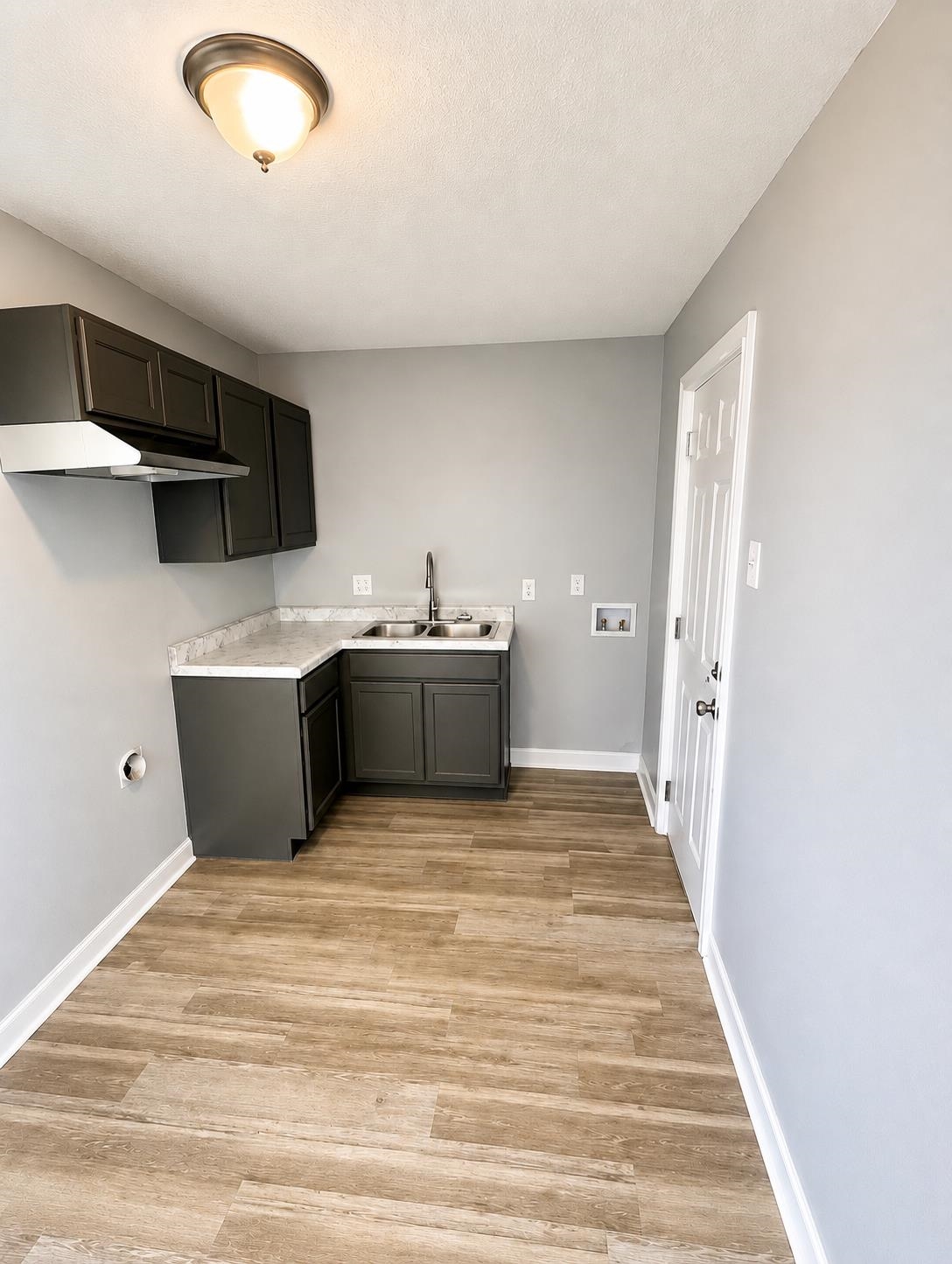 Wood-finish flooring with corner cabinetry, a stainless steel sink, and a wall-mounted range hood