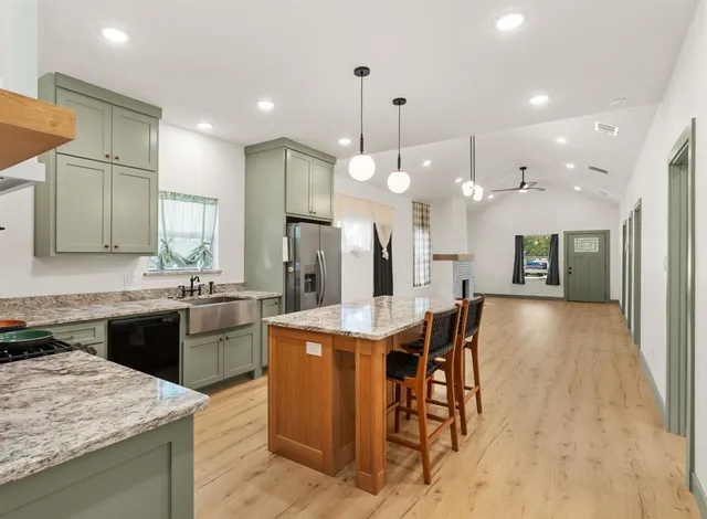 a kitchen with stainless steel appliances kitchen island granite countertop a stove a sink a refrigerator and a dining table with wooden floor