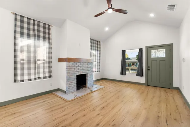 a view of an empty room with wooden floor fireplace and a window