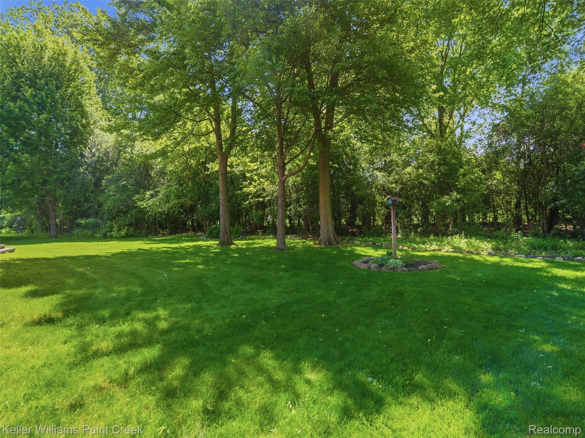 2842 Manorwood Road Troy, MI 48085 - Photo 67 of 72 Expansive green lawn surrounded by mature trees, featuring a central stone-ringed garden bed