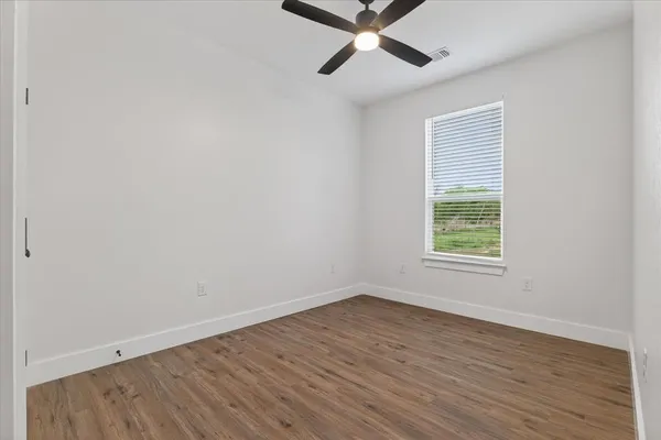 an empty room with wooden floor fan and windows