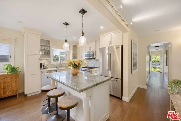 a kitchen with stainless steel appliances granite countertop a refrigerator a oven a sink a dining table and chairs with wooden floor