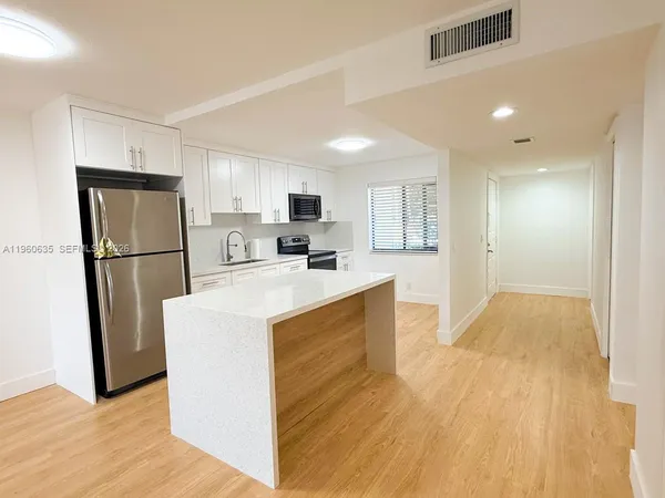 a kitchen with stainless steel appliances granite countertop a refrigerator a sink a stove a microwave and white cabinets with wooden floor