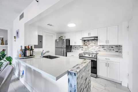 a kitchen with a stove a sink a refrigerator and white cabinets with wooden floor