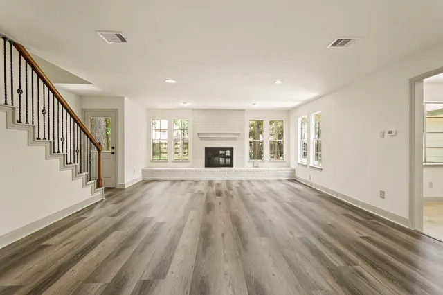 a view of an empty room with wooden floor fireplace and a window