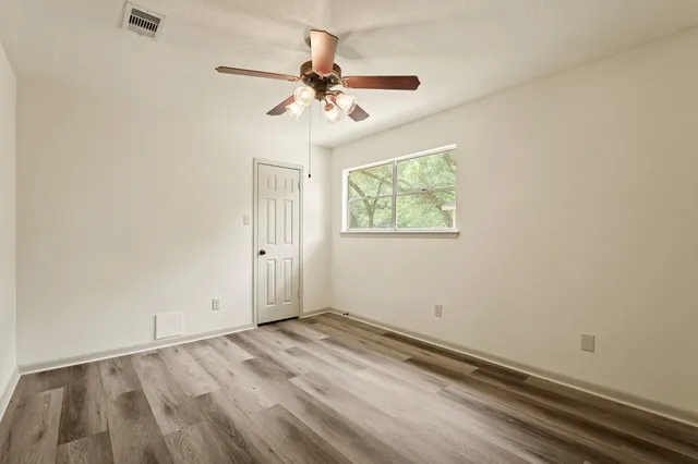 an empty room with wooden floor fan and windows