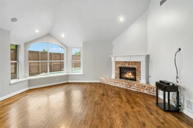 a view of an empty room with wooden floor fireplace and a window