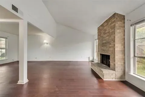 an empty room with wooden floor fireplace and windows