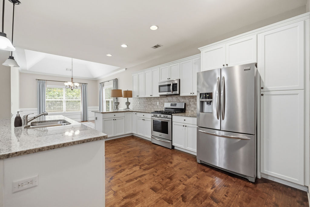 214 Friend Street Anderson, SC 29621 - Photo 9 of 40 This bright kitchen features wood floors and white cabinetry, opening to a dining area with vaulted ceilings.