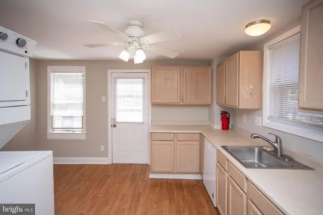 a kitchen with a sink dishwasher a stove and white cabinets with wooden floor