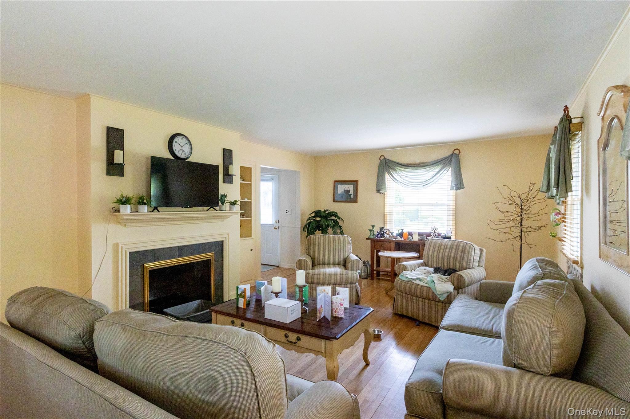 90 Sunset Road Bay Shore, NY 11706 - Photo 16 of 31 Spacious living area featuring warm-toned walls, wood-finish flooring, a fireplace with a black surround and white mantel, and built-in shelving