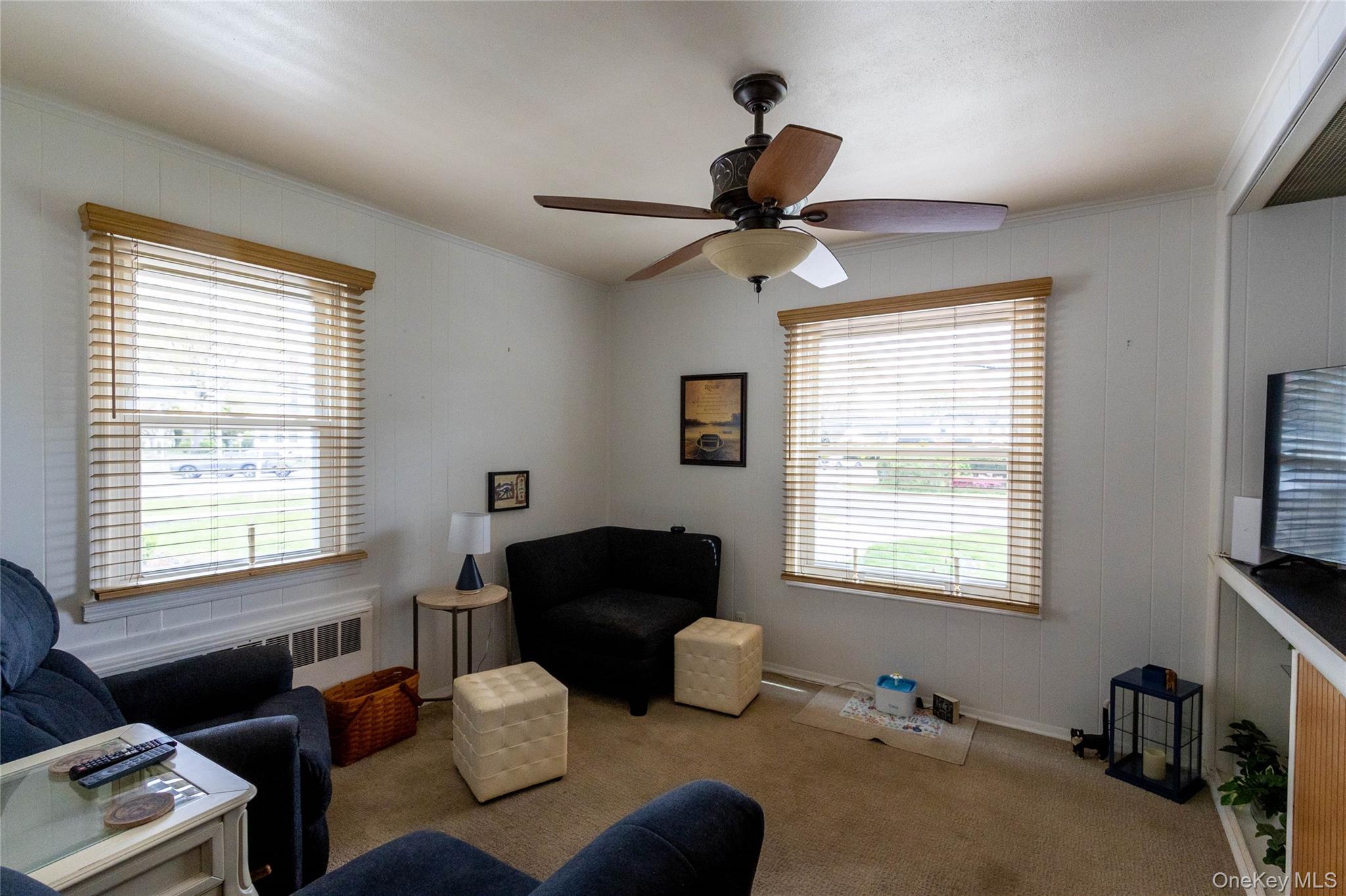 90 Sunset Road Bay Shore, NY 11706 - Photo 23 of 31 Living area featuring two windows with wood-finish blinds, a ceiling fan with integrated lighting, white vertical paneling on the walls, and carpeted flooring