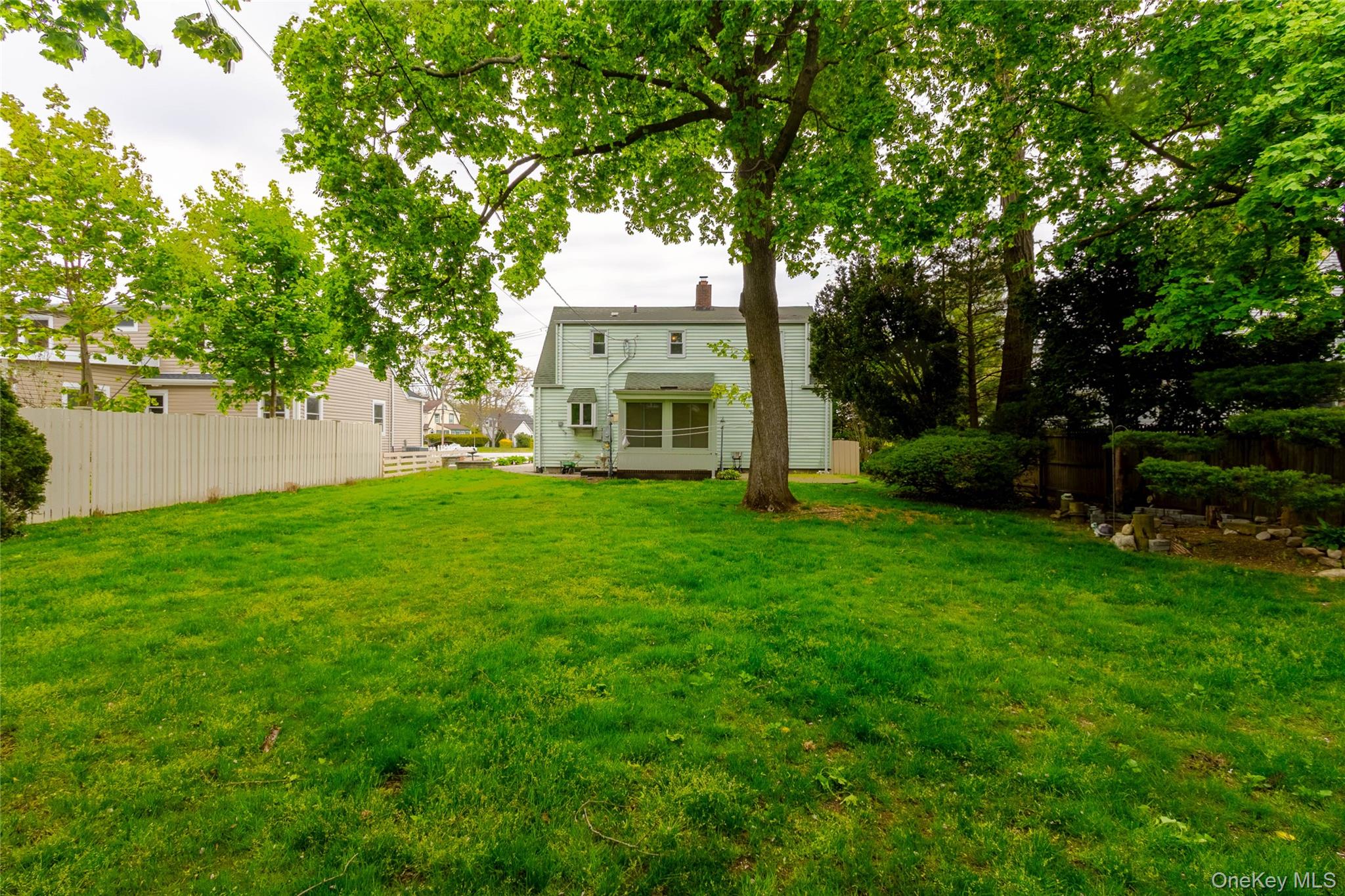 90 Sunset Road Bay Shore, NY 11706 - Photo 8 of 31 Expansive rear yard featuring a large verdant lawn, mature trees, and a white picket fence