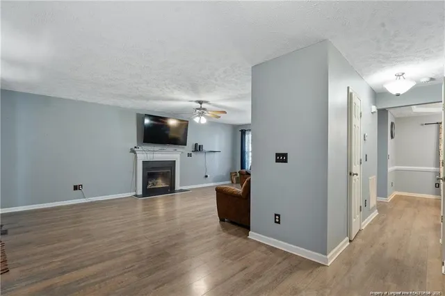 a view of a livingroom with a fireplace a ceiling fan and wooden floor