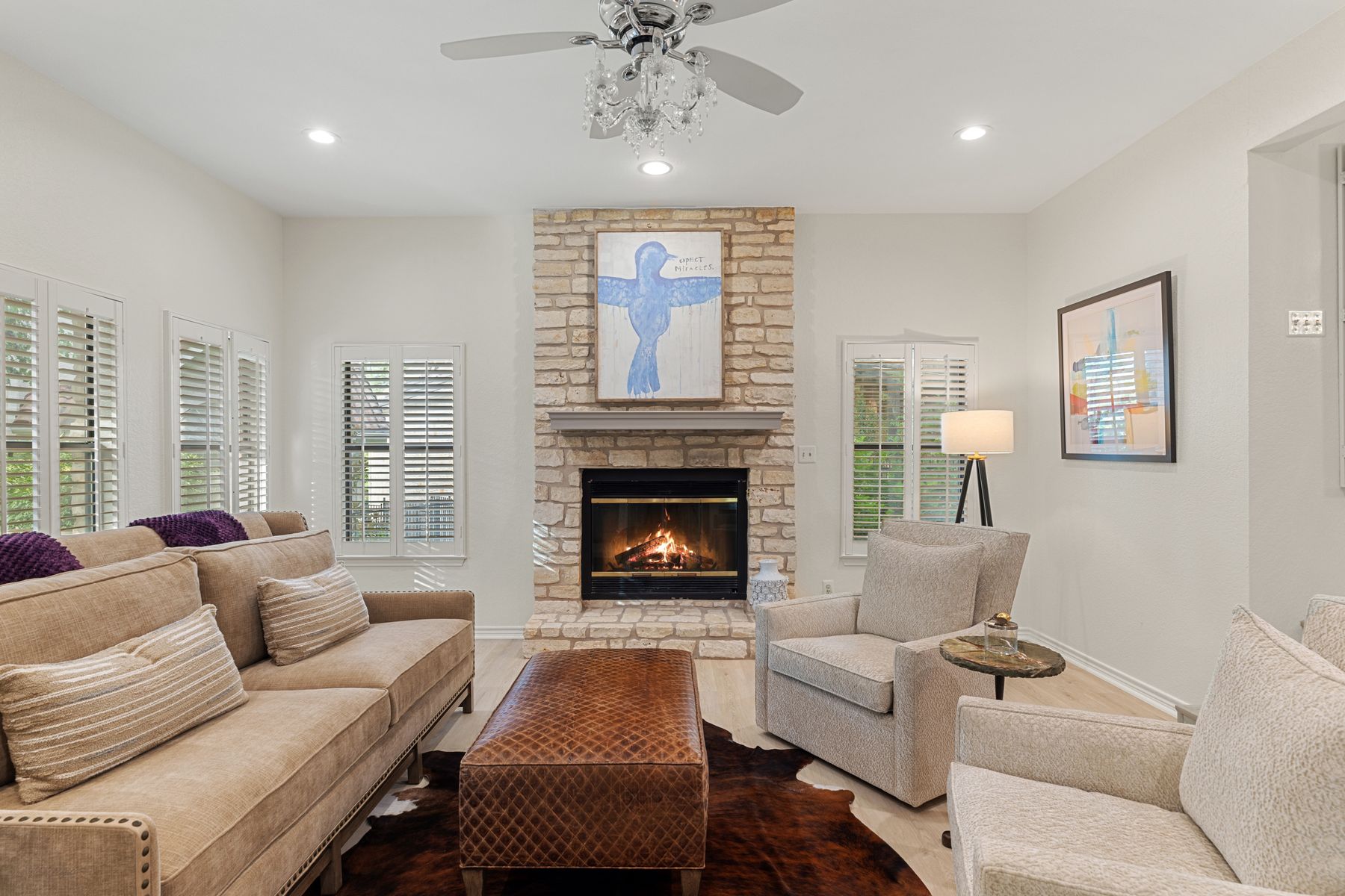5 Valhalla Court The Hills, TX 78738 - Photo 5 of 34 The light-filled living room is both warm and sophisticated, featuring wide-plank flooring, custom built-ins, and a striking floor-to-ceiling stone fireplace as the focal point.