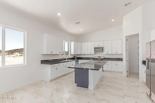 a kitchen with stainless steel appliances granite countertop a stove top oven a sink a refrigerator and white cabinets