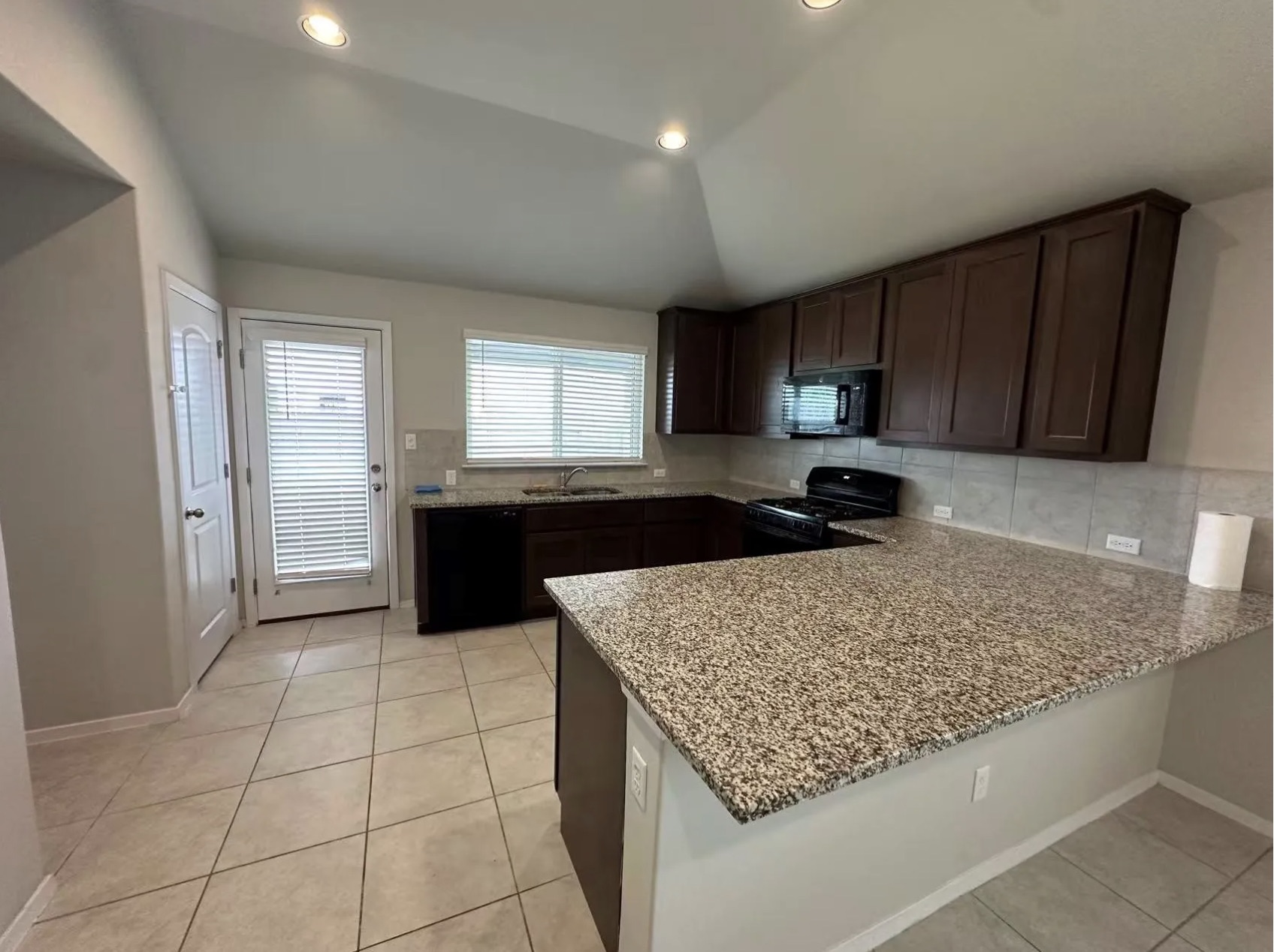 251 Tempest Trail Maxwell, TX 78656 - Photo 12 of 15 Kitchen featuring dark wood finish cabinetry, lofted ceiling, black appliances, light tile patterned flooring, and a peninsula