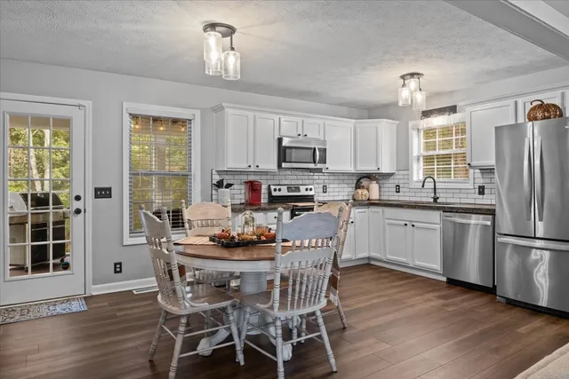 a kitchen with stainless steel appliances granite countertop a stove a refrigerator a sink dishwasher a dining table and chairs with wooden floor