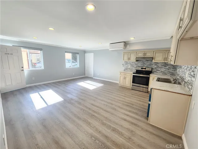 an empty room with wooden floor and kitchen view