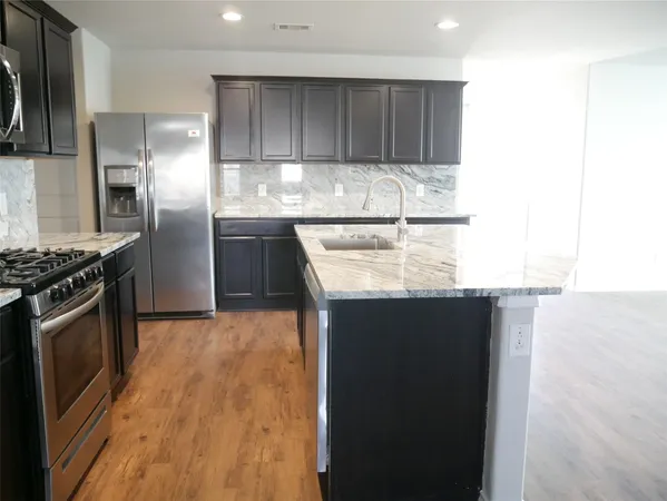 a kitchen with kitchen island granite countertop a stove a refrigerator and a sink