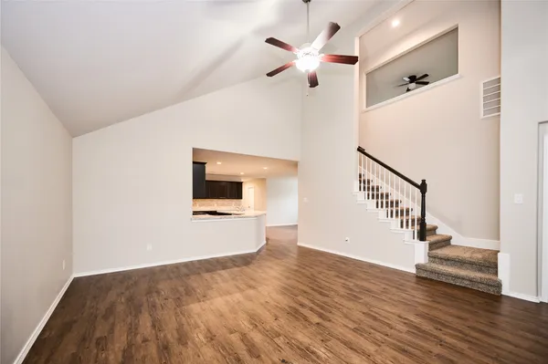 a view of an empty room with wooden floor and a ceiling fan