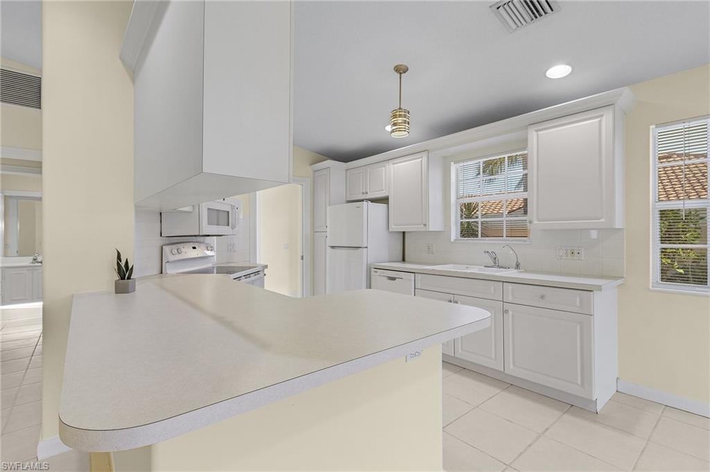 4187 St George Lane Naples, FL 34119 - Photo 7 of 27 Kitchen with kitchen peninsula, white cabinets, pendant lighting, and white appliances