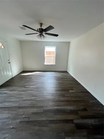 an empty room with wooden floor ceiling fan and windows