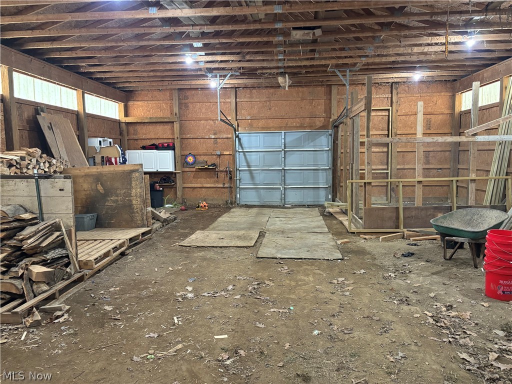 9550 Spencer Road Homerville, OH 44235 - Photo 46 of 50 Spacious barn featuring exposed wood beam ceiling, multiple fluorescent light fixtures, a large roll-up door, and dirt floors.
