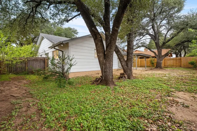 a backyard of a house with plants and large tree