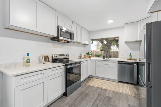 a kitchen with stainless steel appliances granite countertop a sink dishwasher a refrigerator and white cabinets with wooden floor