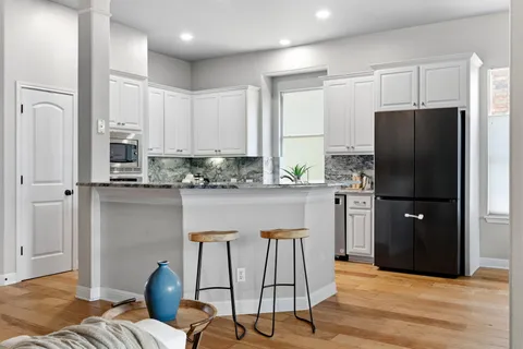 a kitchen with stainless steel appliances granite countertop a refrigerator a stove a sink and white cabinets with wooden floor