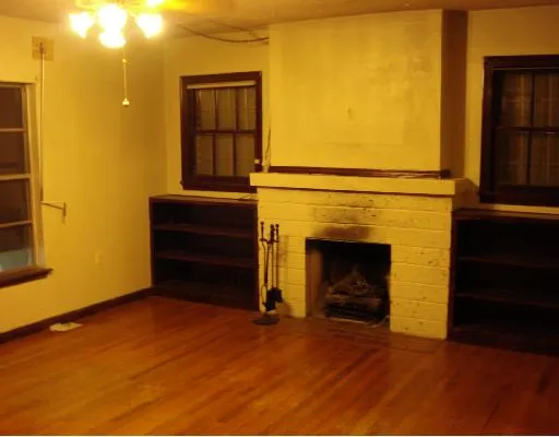 a view of an empty room with wooden floor and a fireplace