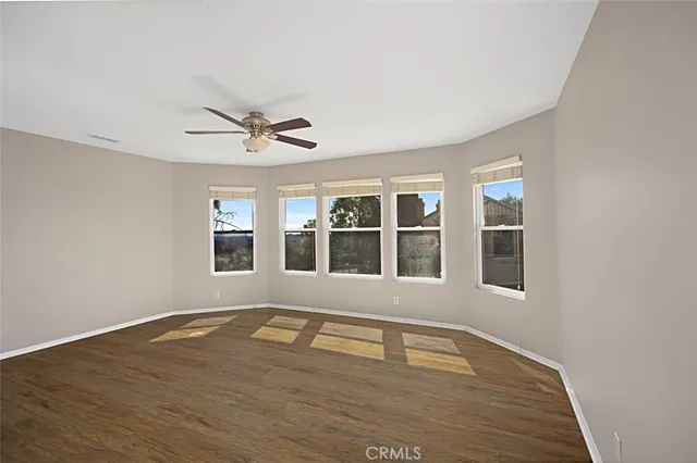 an empty room with wooden floor fan and windows