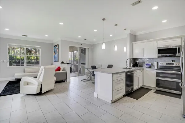 a large white living room with stainless steel appliances kitchen island granite countertop a refrigerator and a sink