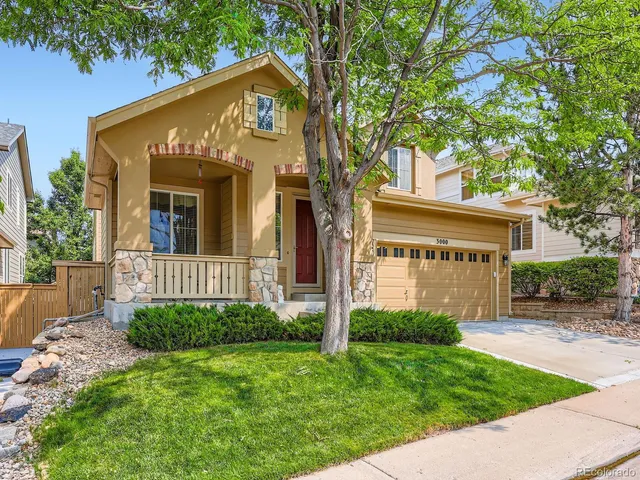 a view of a house with brick walls and a yard with plants and large trees