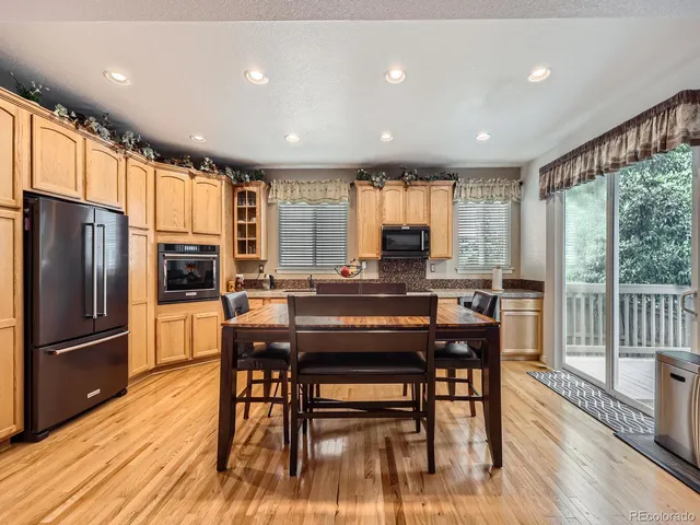 a kitchen with stainless steel appliances granite countertop a stove a refrigerator a sink a dining table and chairs with wooden floor