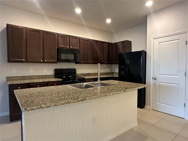 a kitchen with kitchen island granite countertop wooden cabinets and refrigerator