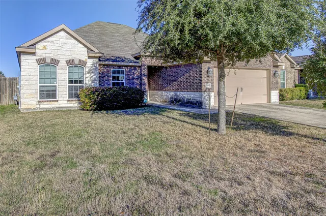 a view of a house with a small yard and a large tree