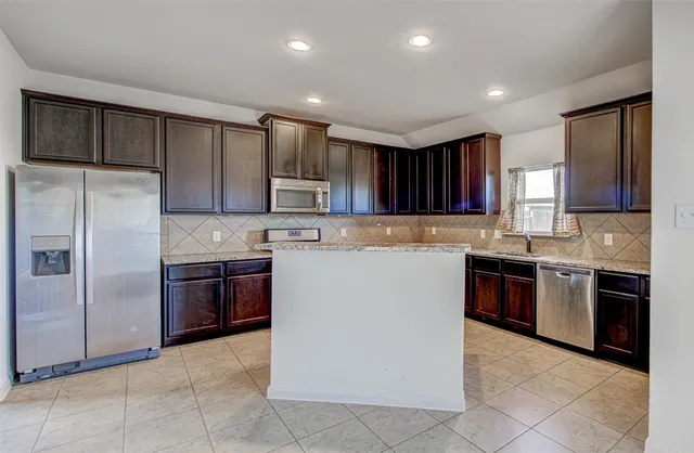 a kitchen with kitchen island granite countertop wooden cabinets a refrigerator and a stove top oven