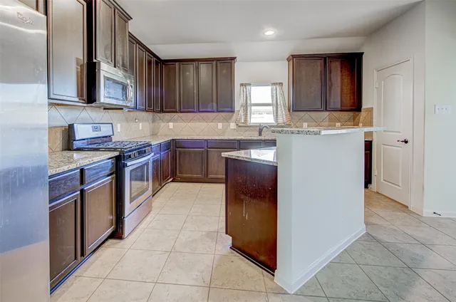 a kitchen with kitchen island granite countertop a stove top oven a sink a counter top space and cabinets