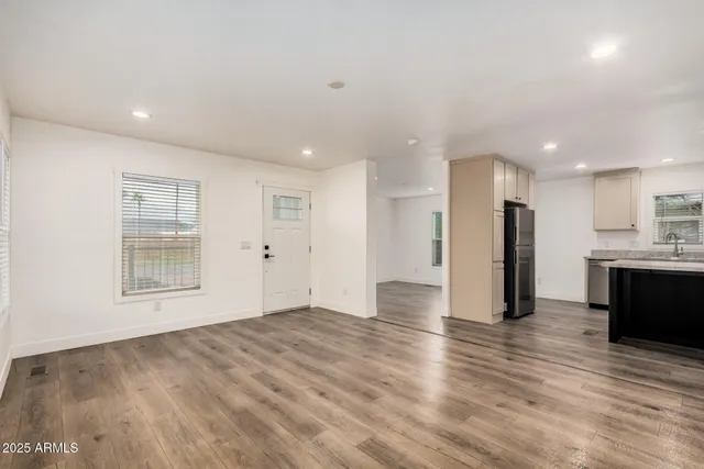 a view of an empty room with wooden floor and a kitchen