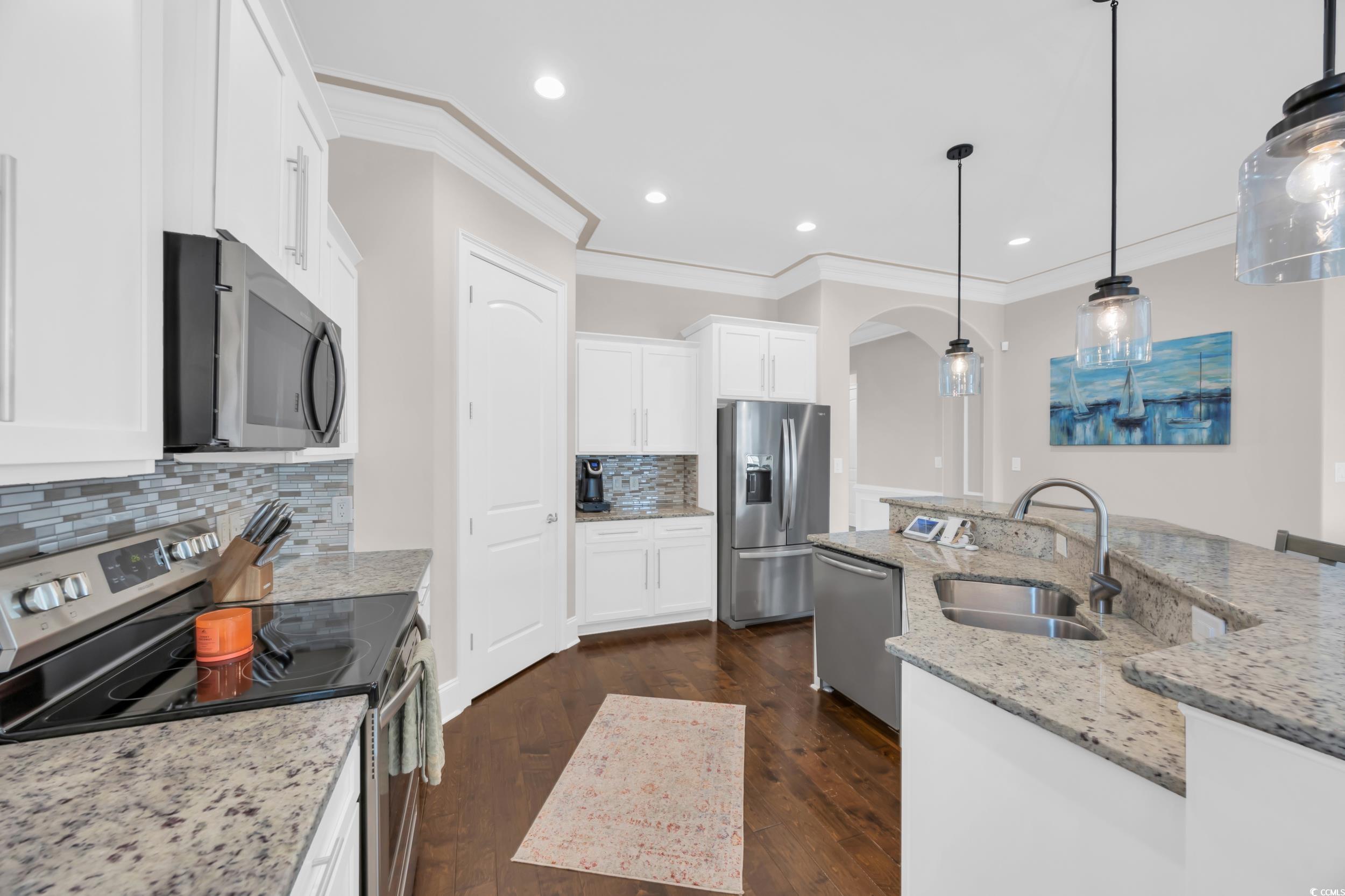 937 Bluffview Drive Myrtle Beach, SC 29579 - Photo 3 of 40 Kitchen featuring appliances with stainless steel finishes, light stone countertops, white cabinetry, crown molding, and dark wood finished floors