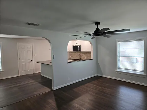 a view of a livingroom with wooden floor a ceiling fan and windows