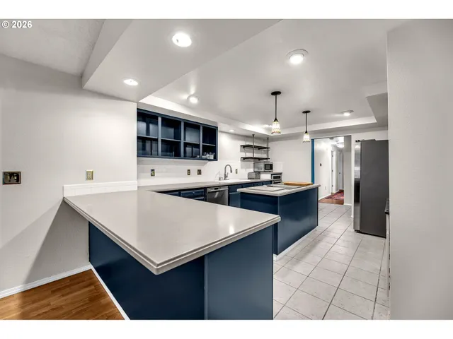a kitchen with stainless steel appliances kitchen island granite countertop a refrigerator a stove a sink dishwasher and white cabinets with wooden floor