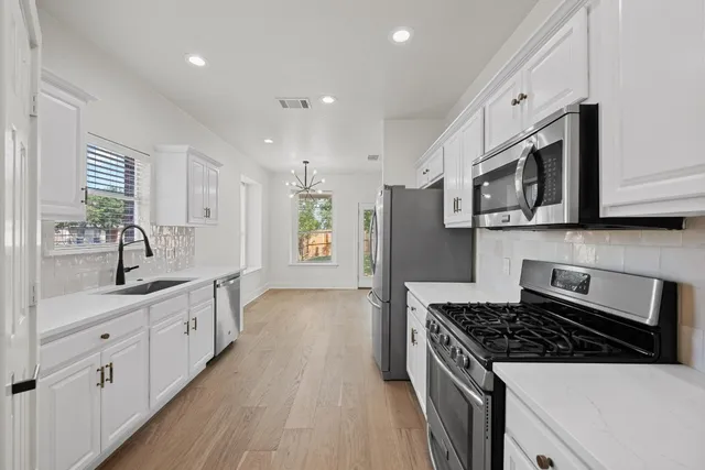 a kitchen with stainless steel appliances a sink dishwasher stove refrigerator and white cabinets with wooden floor