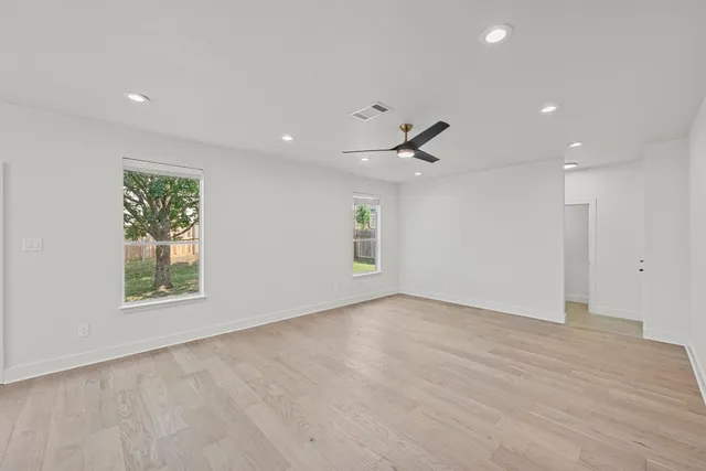 an empty room with wooden floor ceiling fan and windows