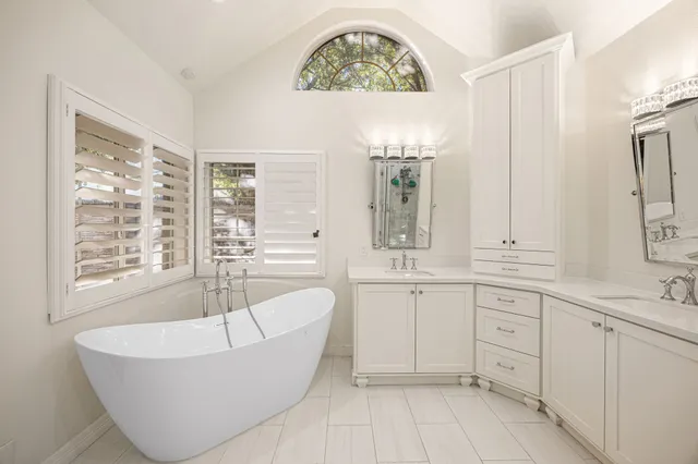 a spacious bathroom with a double vanity sink a mirror a bathtub and next to a window