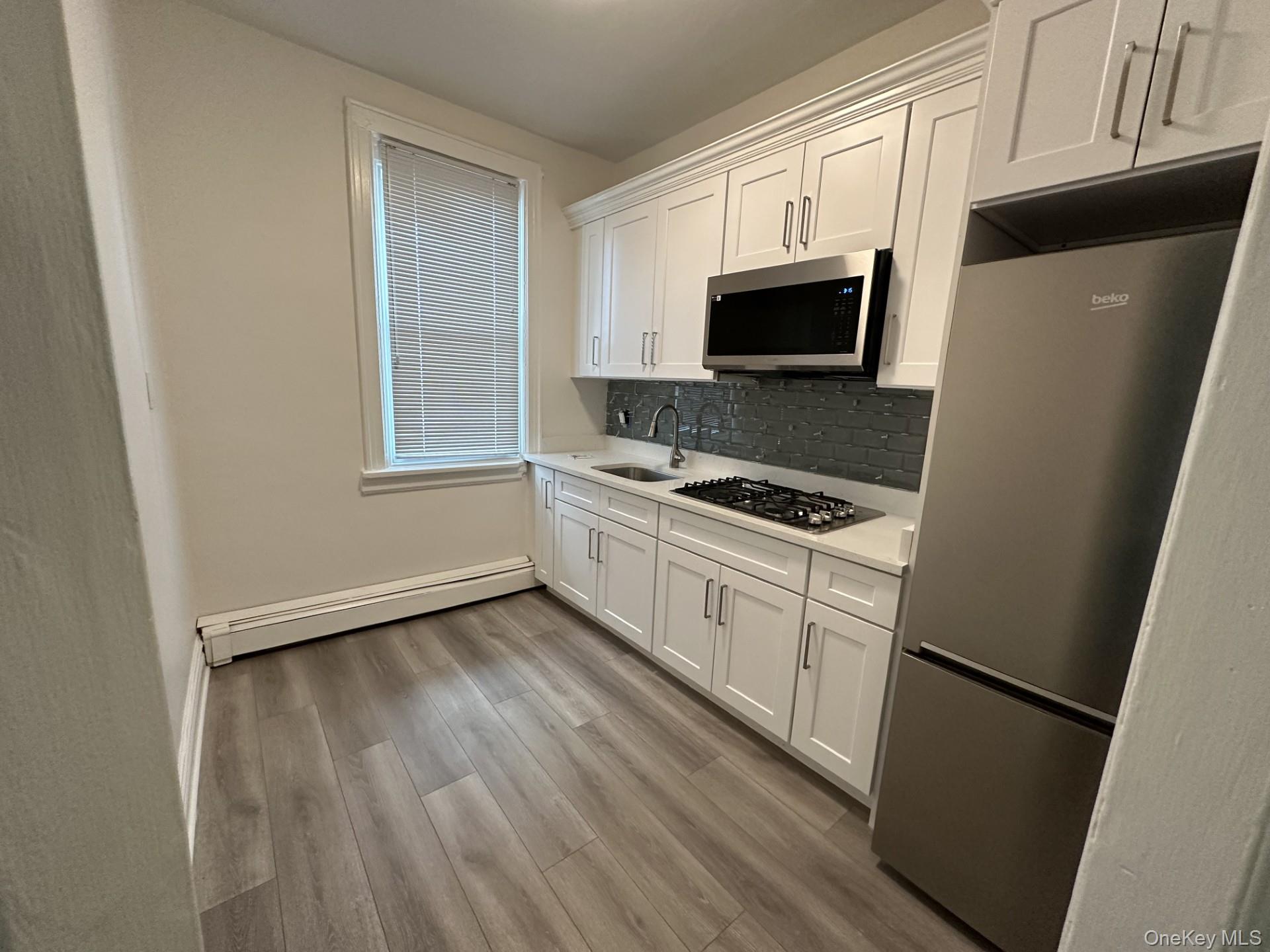 117 Plandome Road, Unit 2R Manhasset, NY 11030 - Photo 7 of 13 Kitchen with stainless steel appliances, white cabinets, a baseboard heating unit, and light wood-style floors